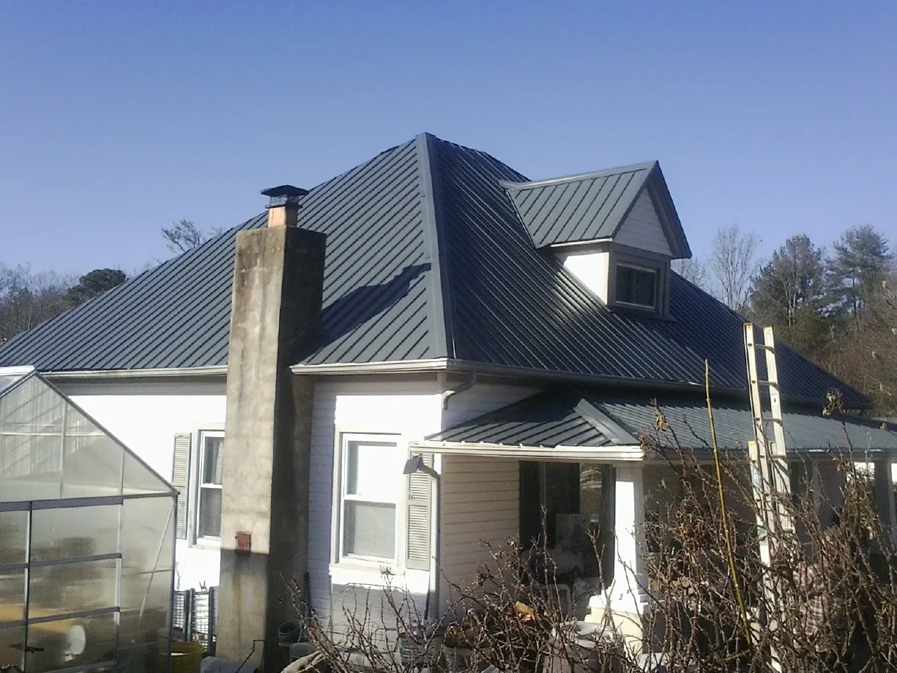 Dark blue standing seam metal roof on a white farmhouse with dormer — Slate & Tile Roof Repair by Roofing Brothers in Halstad