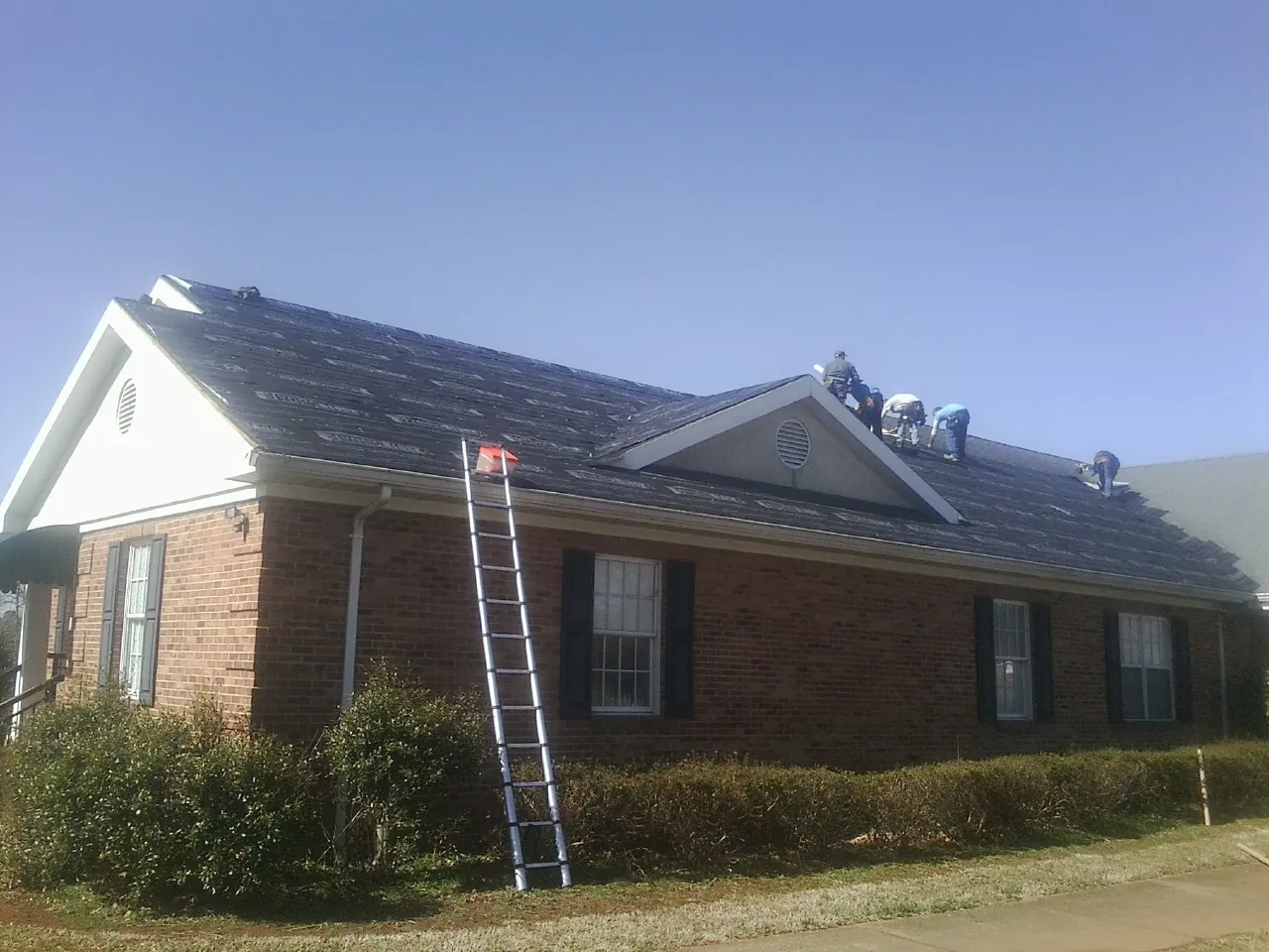 Crew tearing shingles off a brick ranch roof with a ladder set — Metal Roof Repair work by our crew in Halstad