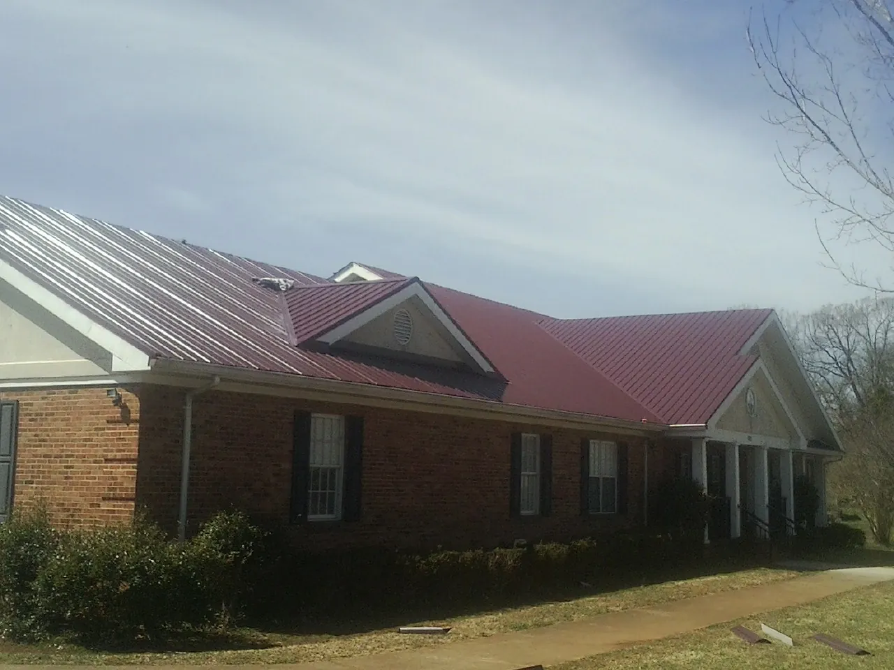 Red metal roof with gabled entries on a long brick building, from a Hail Damage Roof Repair job in Halstad