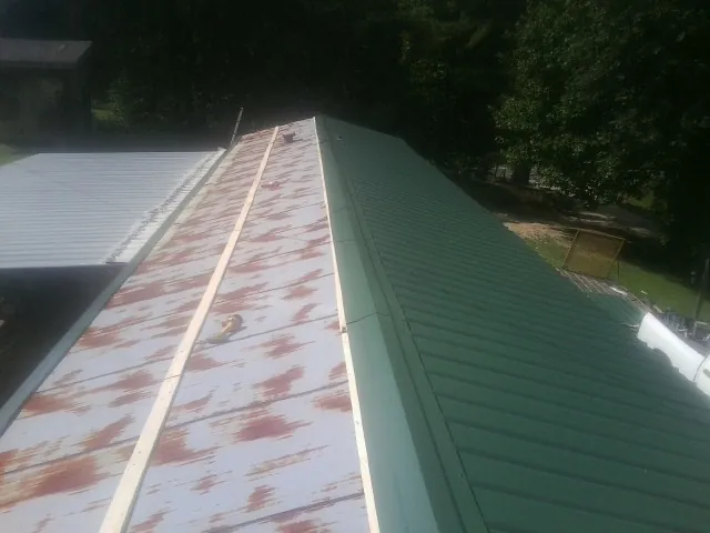 Old rusted panels beside newly installed green metal roofing — Wind Damage Roof Repair by Roofing Brothers in Halstad
