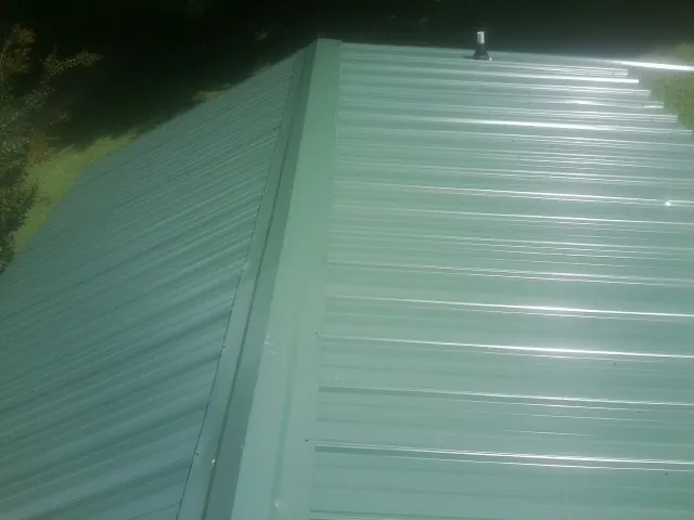 New green metal panels meeting at the ridge of a roof — Flat Roof Repair work by our crew in Halstad