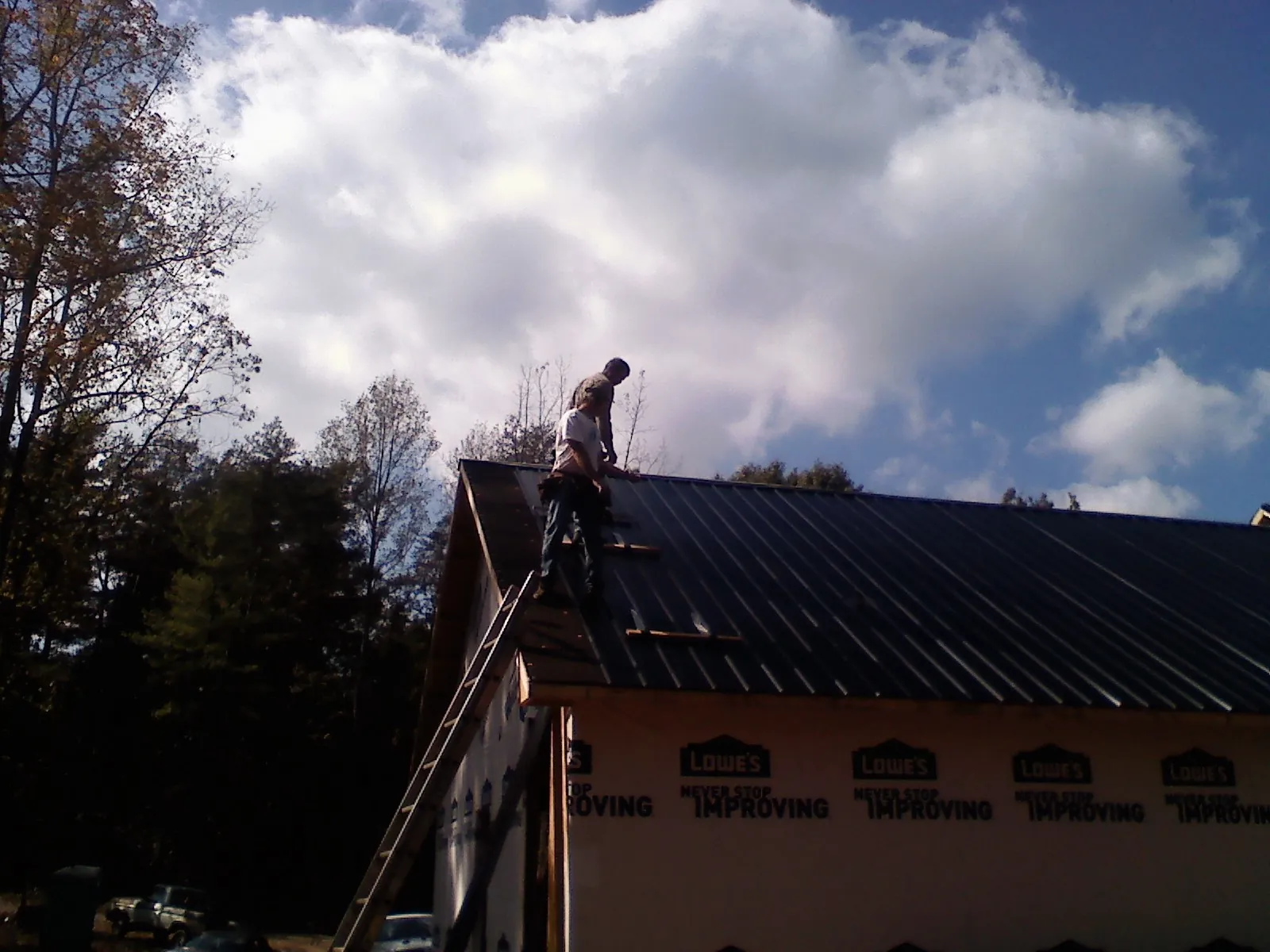 Roofer fastening dark metal panels high against a cloudy sky, from a Roof Inspection job in Halstad